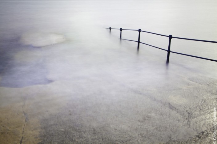 piscine d'eau de mer remplie avec la marée laissant apparaitre la rambarde de protection. Prise de vue en pose longue à Guernesey, Royaume Uni.