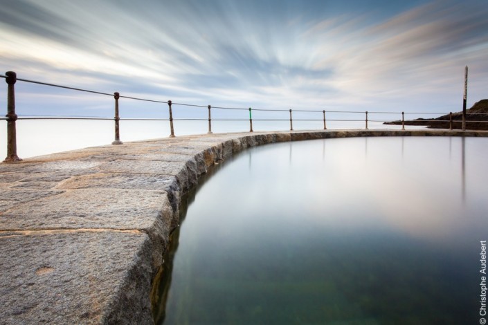 piscine d'eau de mer remplie avec la marée laissant apparaitre à moitié deux échelles et la rambarde de protection. Prise de vue en pose longue à Guernesey, Royaume Uni.