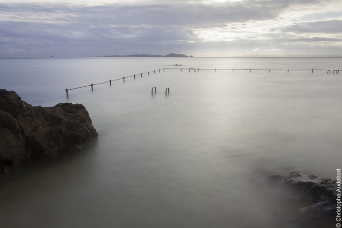piscine d'eau de mer remplie avec la marée laissant apparaitre à moitié deux échelles et la rambarde de protection. Prise de vue en pose longue à Guernesey, Royaume Uni.